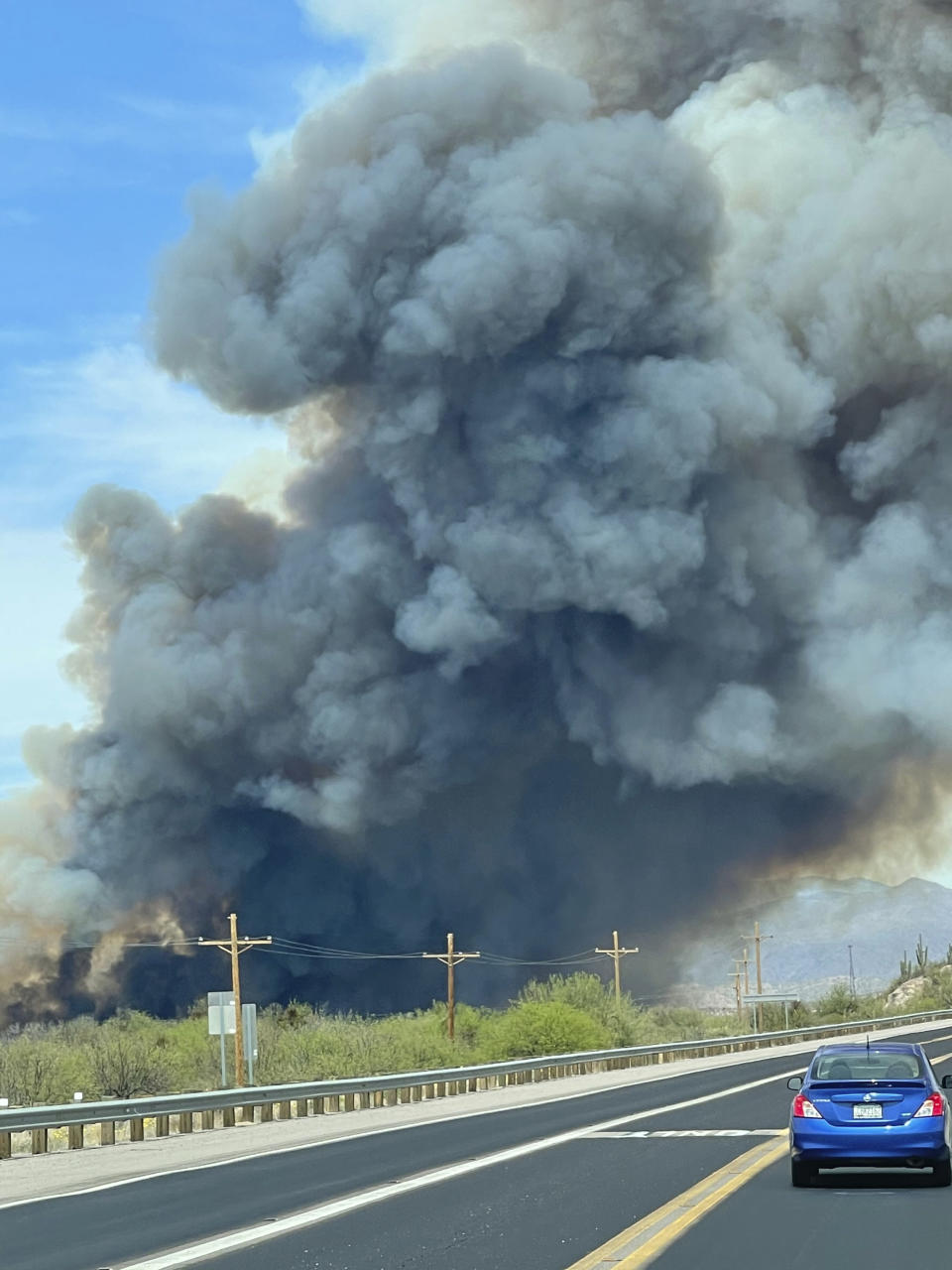 In this Thursday, April 8, 2021, photo provided by Arizona Department of Forestry & Fire Management, a vehicle drive by a plume of smoke from the Pinal County Wildfire burning near in Dudleyville, Ariz. A small community in south-central Arizona remained under an evacuation notice Friday after crews and air tankers stopped the growth of a wildfire that burned at least 12 homes, officials said. (Arizona Department of Forestry & Fire Management via AP)