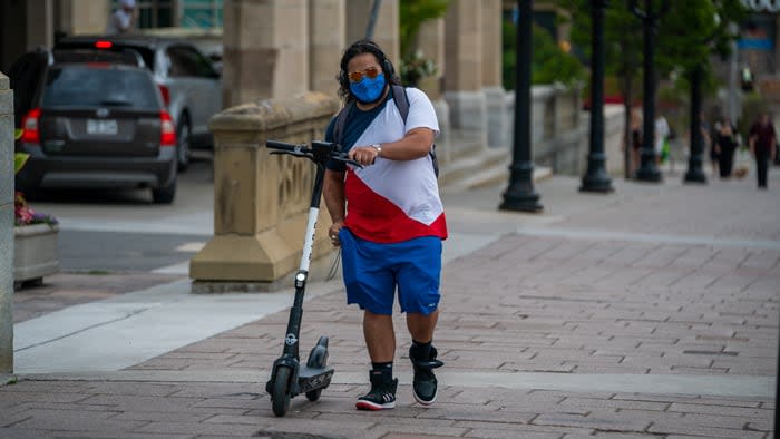 Someone walks an e-scooter on a downtown Ottawa street in July 2020, the first year of the province's e-scooter pilot project. (Michel Aspirot/Radio-Canada - image credit)