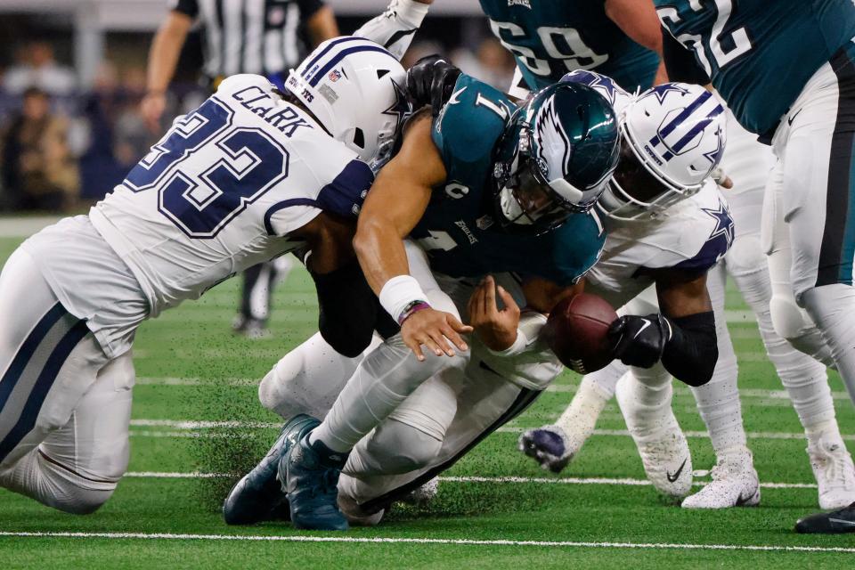 Dallas Cowboys safety Donovan Wilson, right, forces a fumble by Philadelphia Eagles quarterback Jalen Hurts, center, as teammate Damone Clark (33) helps apply pressure during the first half of an NFL football game, Sunday, Dec. 10, 2023, in Arlington, Texas. The Cowboys recovered the ball on the play. (AP Photo/Michael Ainsworth)