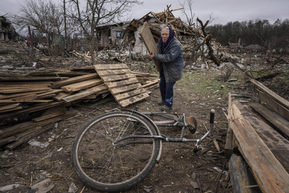 A woman collects wooden planks in a street destroyed by shellings in Chernihiv, Ukraine, Wednesday, April 13, 2022. (AP Photo/Evgeniy Maloletka)