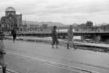 People walk over Aioi Bridge as the gutted Hiroshima Prefectural Industrial Promotion Hall (L), currently known as Atomic Bomb Dome or A-Bomb Dome, is seen in the background after the atomic bombing of Hiroshima, Japan, on August 6, 1945, in this handout photo taken by Shigeo Hayashi in October 1945 and released by Hiroshima Peace Memorial Museum. REUTERS/Shigeo Hayashi/Hiroshima Peace Memorial Museum/Handout via Reuters