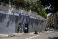 In this Wednesday, May 13, 2020 photo, a bank customer leaves from the main door as a worker installs iron shields along the facade to prevent acts of sabotage in Beirut, Lebanon. Riad Salameh, Lebanon’s long-serving central bank governor, was touted as the guardian of Lebanon’s monetary stability as he steered the tiny country's finances through post-war recovery and various bouts of unrest for nearly three decades. Now he is being called a “thief” by some protesters, who accuse him of being part of the ruling elite whose corruption and mismanagement has driven the country to the edge of bankruptcy. (AP Photo/Hassan Ammar)