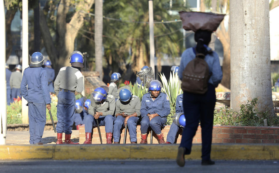 People walk past armed riot police in Harare, Friday, Aug. 16, 2019. Zimbabwe's police patrolled the streets of the capital Friday morning while many residents stayed home fearing violence from an anti-government demonstration planned by the opposition. (AP Photo/Tsvangirayi Mukwazhi)