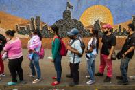 Des Vénézuéliens font la queue à un arrêt de bus devant une fresque murale représentant l'Assemblée nationale, le 2 décembre 2020 à Caracas