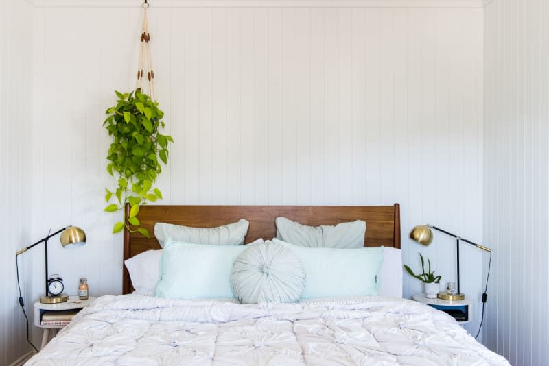 A white bedroom with vertical beadboard and planter hung from the ceiling