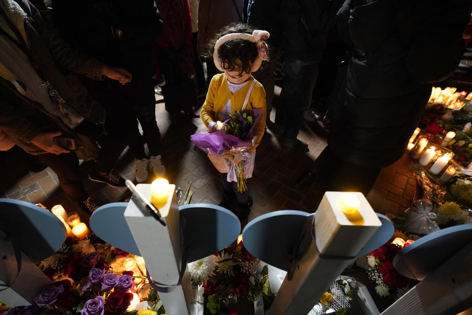 A girl holds flowers near wooden hearts displaying names of victims at a vigil outside Monterey Park City Hall, blocks from the Star Ballroom Dance Studio, late Tuesday, Jan. 24, 2023, in Monterey Park, Calif. A gunman killed multiple people at the ballroom dance studio late Saturday amid Lunar New Year's celebrations in the predominantly Asian American community. (AP Photo/Ashley Landis)