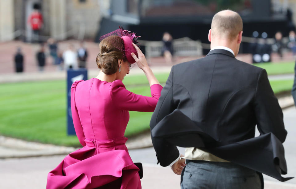 Kate Middleton grabs her fascinator as Prince William’s coattails fly up. (Photo: Getty Images)