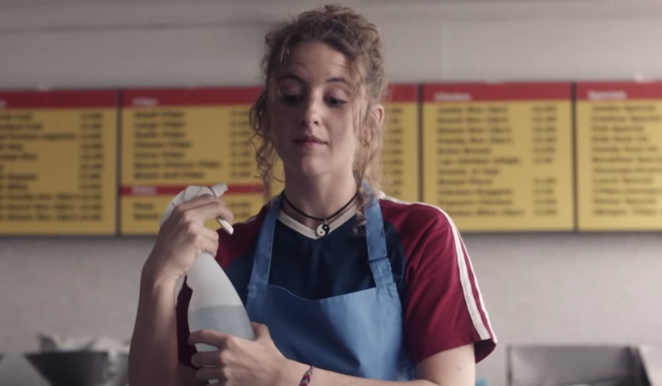 Louisa Harland as Orla, spraying herself with a spray bottle