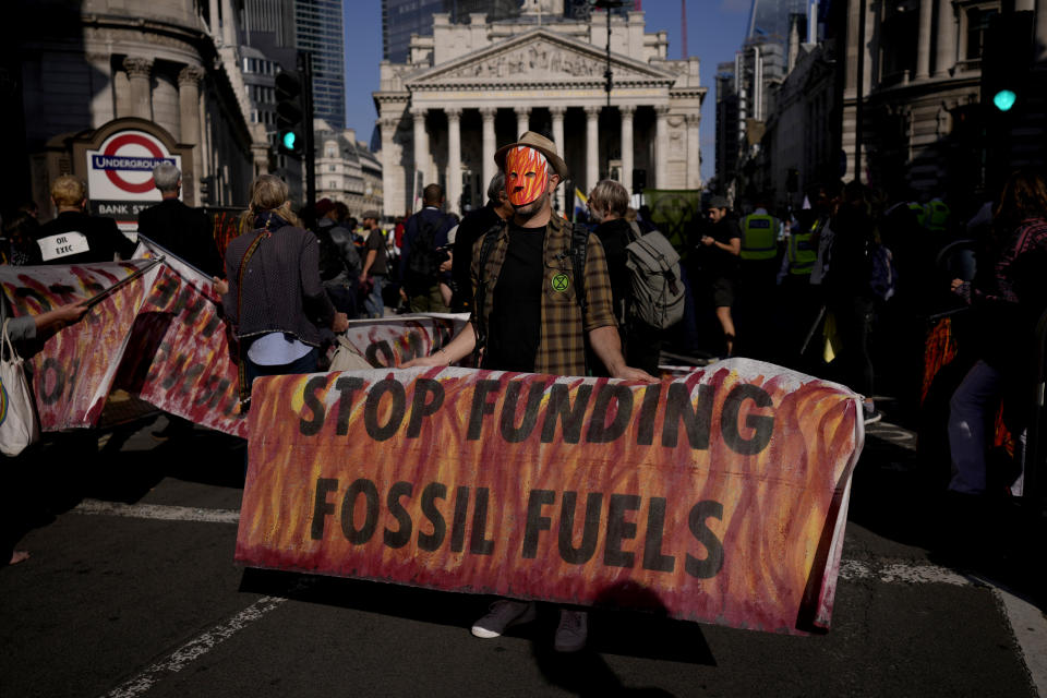 FILE - In this Thursday, Sept. 2, 2021 file photo, an Extinction Rebellion climate change activist holds a banner backdropped by the Bank of England, at left, and the Royal Exchange, center, in the City of London financial district in London. According to a study from University College London climate scientists released on Wednesday, Sept. 8, 2021, strict limits on amounts of fossil fuels extracted from the ground are needed to meet climate goals of the Paris Climate Agreement. (AP Photo/Matt Dunham)