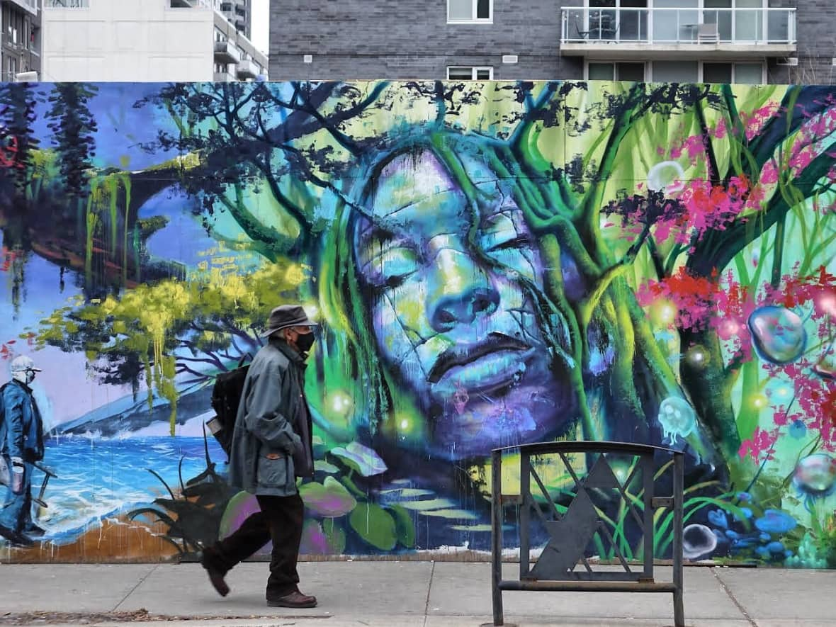 A man wearing a mask walks past a mural in Ottawa on Nov. 30, 2021, during the COVID-19 pandemic.  (Ian Black/CBC - image credit)