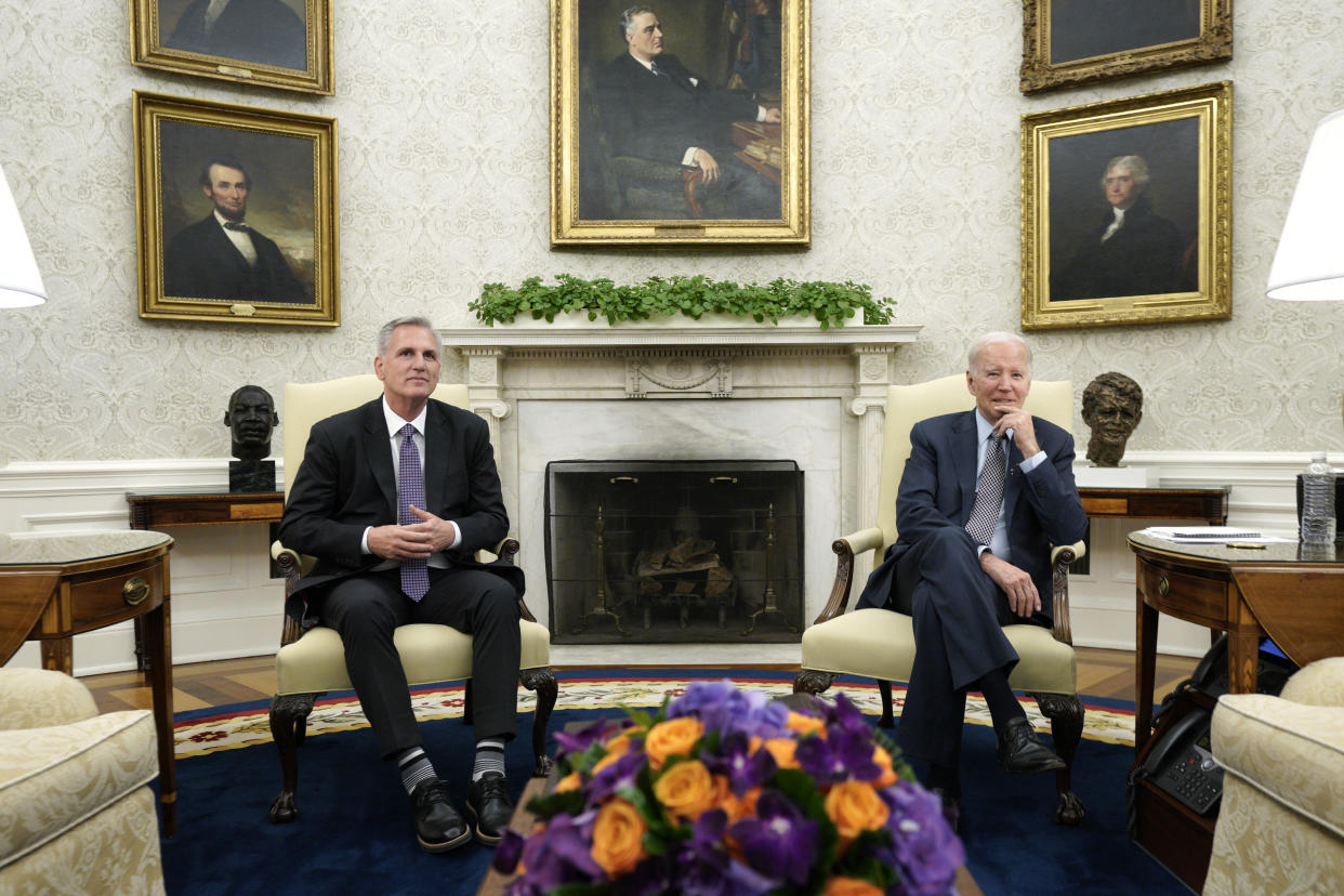 House Speaker Kevin McCarthy and President Biden seated in chairs on either side of a fireplace in the Oval Office.