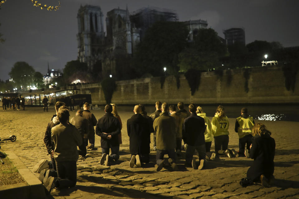 People pray on their knees by the Seine riverside in front of the Notre Dame cathedral in Paris, Tuesday, April 16, 2019. The inferno that raged through Notre Dame Cathedral for more than 12 hours destroyed its spire and its roof but spared its twin medieval bell towers, and a frantic rescue effort saved the monument's "most precious treasures," including the relic revered as Jesus' Crown of Thorns, officials said Tuesday. (AP Photo/Francisco Seco)