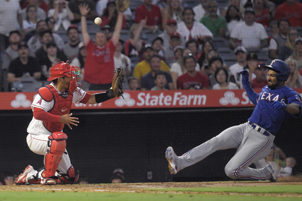 Texas Rangers' Marcus Semien, right, scores after hitting a double and then advancing to home on a fielding error by left fielder Jo Adell as Los Angeles Angels catcher Kurt Suzuki fumbles the ball during the sixth inning of a baseball game Friday, July 29, 2022, in Anaheim, Calif. (AP Photo/Mark J. Terrill)