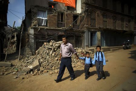 Birendra Karmacharya (L) walks past the debris of collapsed houses while holding the hand of his younger son Saksham Karmacharya, 4, along with his elder son Biyon Karmacharya (R), 9, as they head towards the school, a month after the April 25 earthquake in Bhaktapur, Nepal May 31, 2015. REUTERS/Navesh Chitrakar
