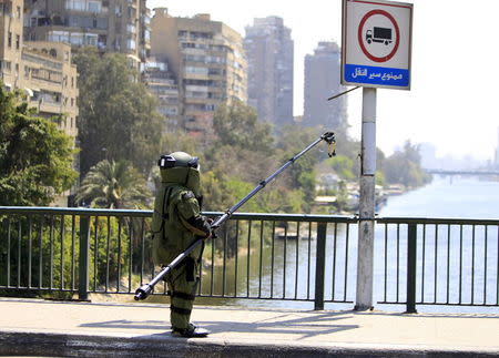 A bomb detonation expert in his suit, accompanied by security personnel (obscured), checks the area after a bomb exploded on a bridge in the Cairo district of Zamalek, April 5, 2015. REUTERS/Mohamed Abd El Ghany