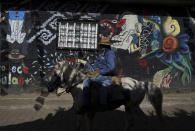 A farmer rides his horse past a mural in the Puerpecha Indigenous community of Comachuen, Mexico, Wednesday, Jan. 19, 2022, where the men are back in town because of the seasonal lull in agricultural work in the United States. Hundreds of men here work at the same vegetable farm in upstate New York every year, planting onions, harvesting squash, cabbage and beans. (AP Photo/Fernando Llano)