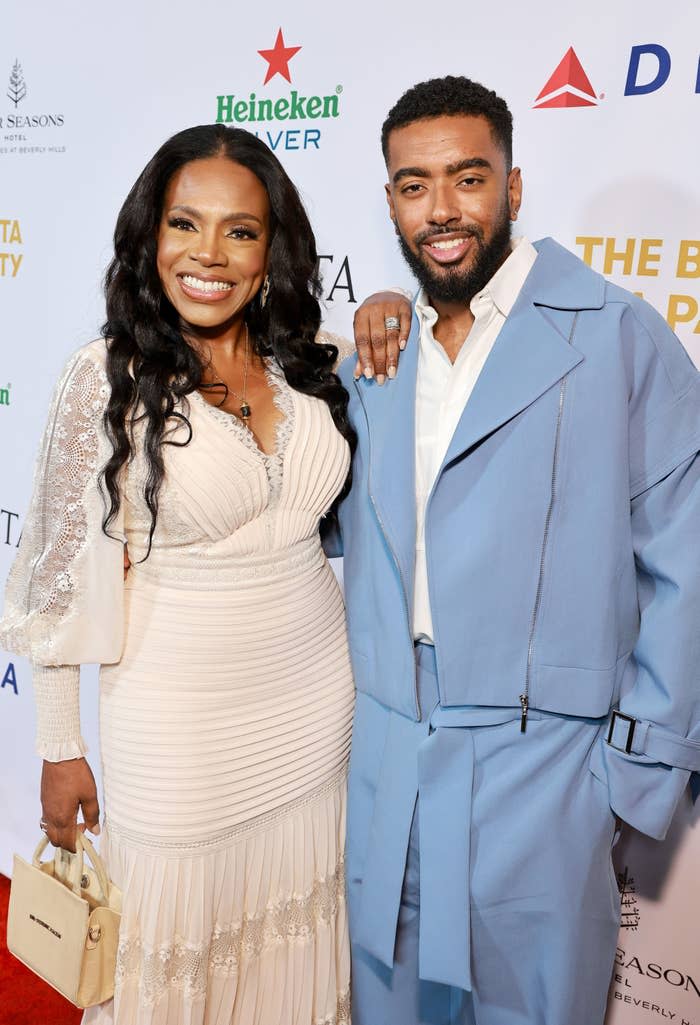 Sheryl Lee Ralph in a long-sleeved lace dress and her son Etienne Maurice in a light suit smile together on the red carpet at an event