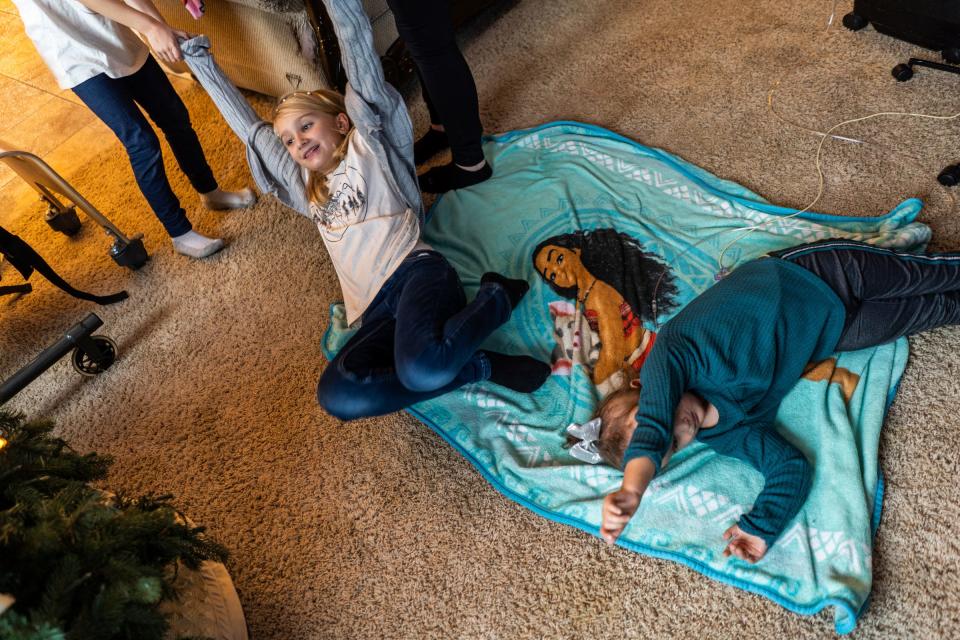 Adelina Calleja, 9, of Livonia, is pulled back into the kitchen by her sister, Evelyn Calleja, 6, and mother, Jewel Calleja, to take part in a tea party as her sister, CC Calleja, right, lays on the floor in the living room of their home in Livonia on Dec. 22, 2023. CC was born with Trisomy 18 and despite intense pressure to terminate the pregnancy, the Callejas say CC is now 4 years old and a valued and interactive member of the family.