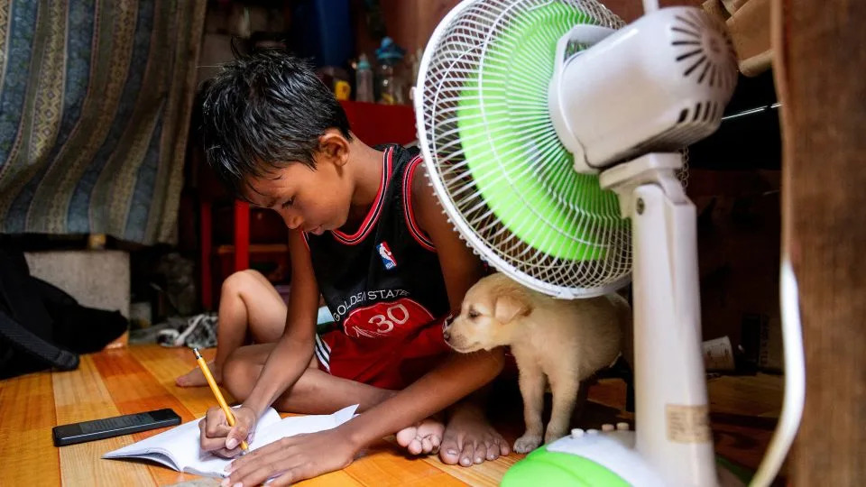 A student doing school work at home in front of a fan following the suspension of in-person classes because of the heat, in Manila, Philippines, April 26, 2024. - Lisa Marie David/Reuters