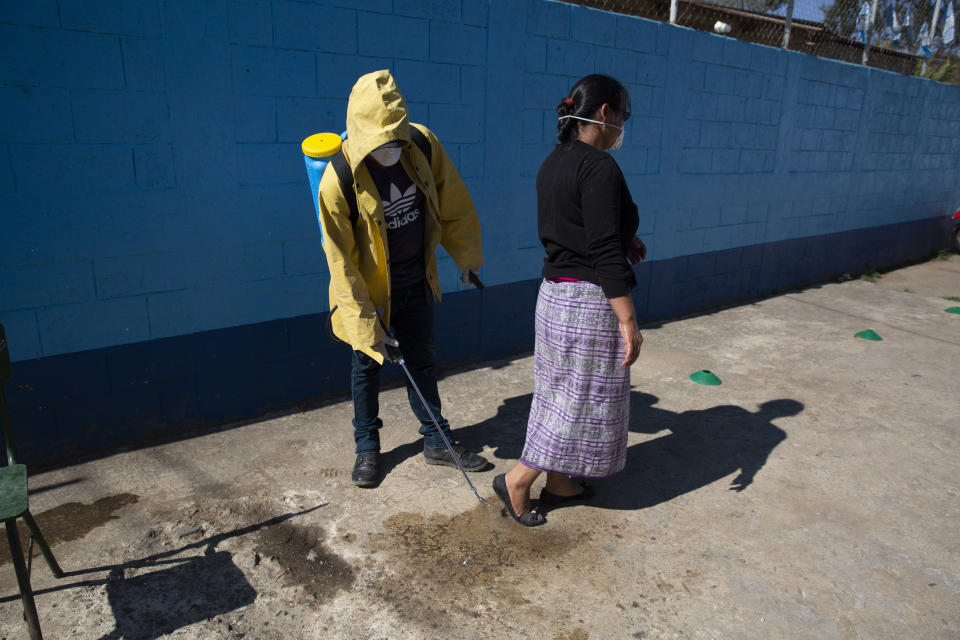 Un trabajador con equipo de protección rocía un desinfectante en la parte inferior de los zapatos de una mujer como precaución contra la propagación del nuevo coronavirus antes de ingresar a la escuela de su hijo en San Martín Jilotepeque, Guatemala, el viernes 3 de abril de 2020. (Foto AP/Moisés Castillo)