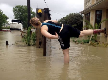 A woman stands on one leg, water pouring out of her other boot, as she looks at a partially submerged truck on a street flooded after heavy rains in Sochi, Russia, June 25, 2015. REUTERS/Kazbek Basaev