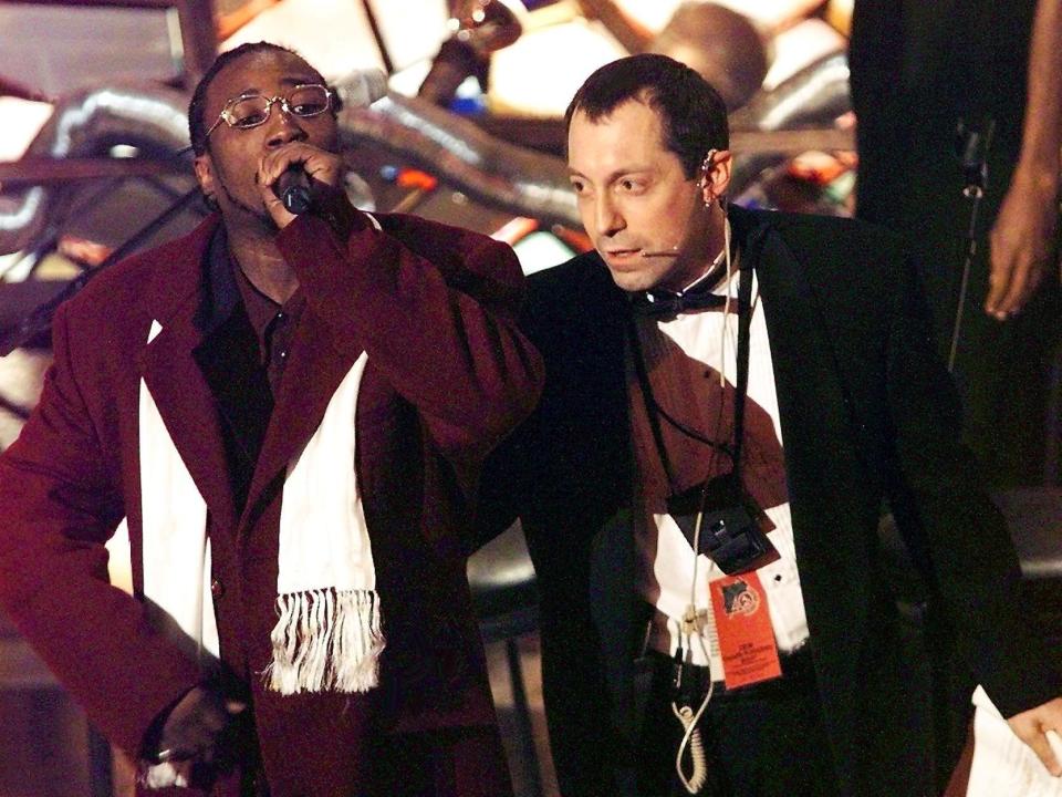 The Wu-Tang singer speaking into a microphone while a Grammys employee tries to escort him off the stage.