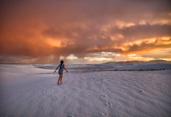 Person wandering through sand dunes at sunset