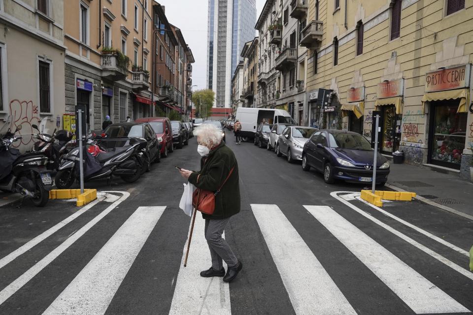 An elderly woman crosses a street in Milan, Italy, Tuesday, Dec. 1, 2020. In Italy, which has the world's second-oldest population, many people in their 70s and older have kept working through the COVID-19 pandemic. From neighborhood newsstand dealers to farmers bring crops to market, they are defying stereotypic labels that depict the old as a monolithic category that's fragile and in need of protection. (AP Photo/Luca Bruno)