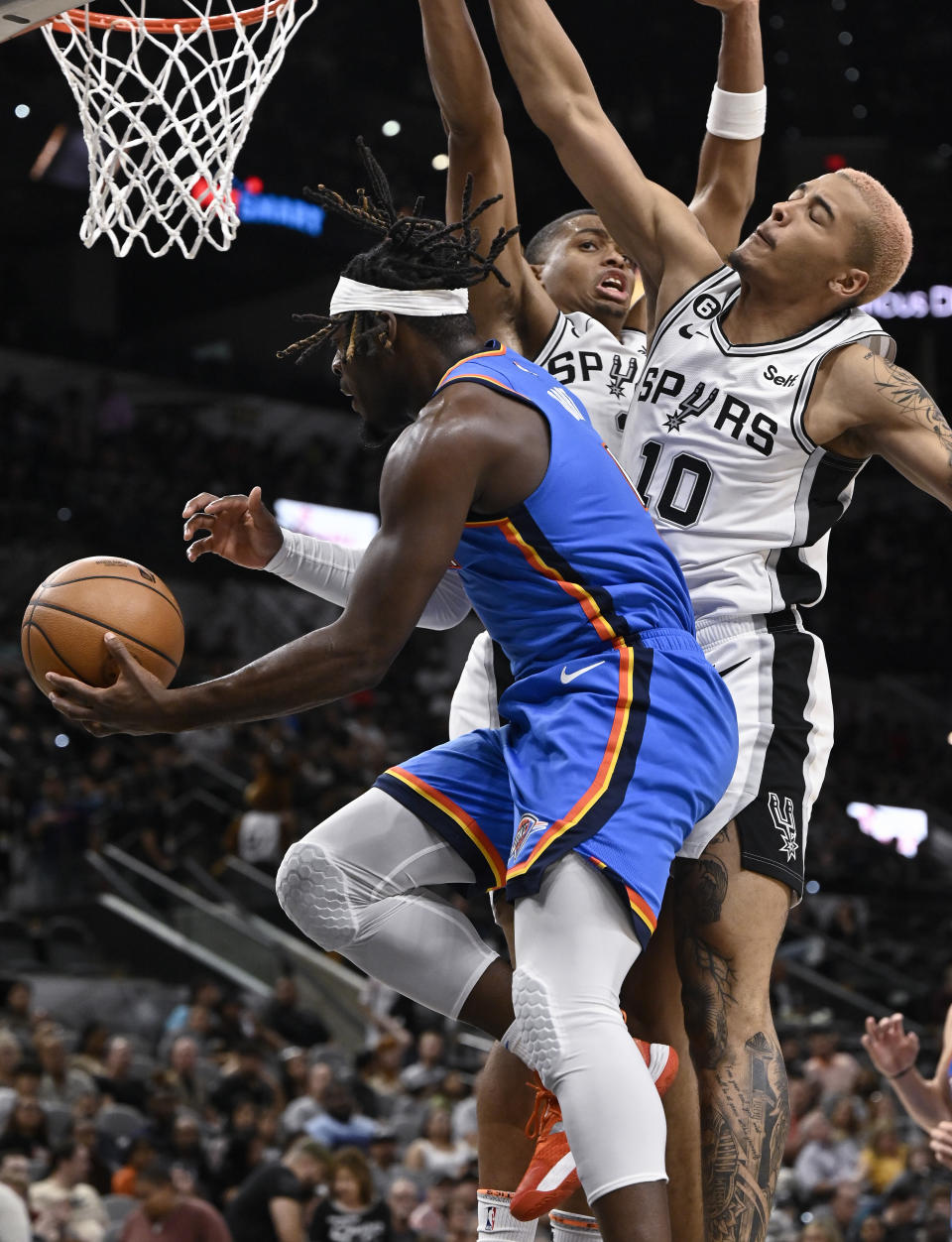 Oklahoma City Thunder's Luguentz Dort, left, goes to the basket while defended by San Antonio Spurs' Jeremy Sochan (10) and Keldon Johnson during the first half of a preseason NBA basketball game Thursday, Oct. 13, 2022, in San Antonio. (AP Photo/Darren Abate)