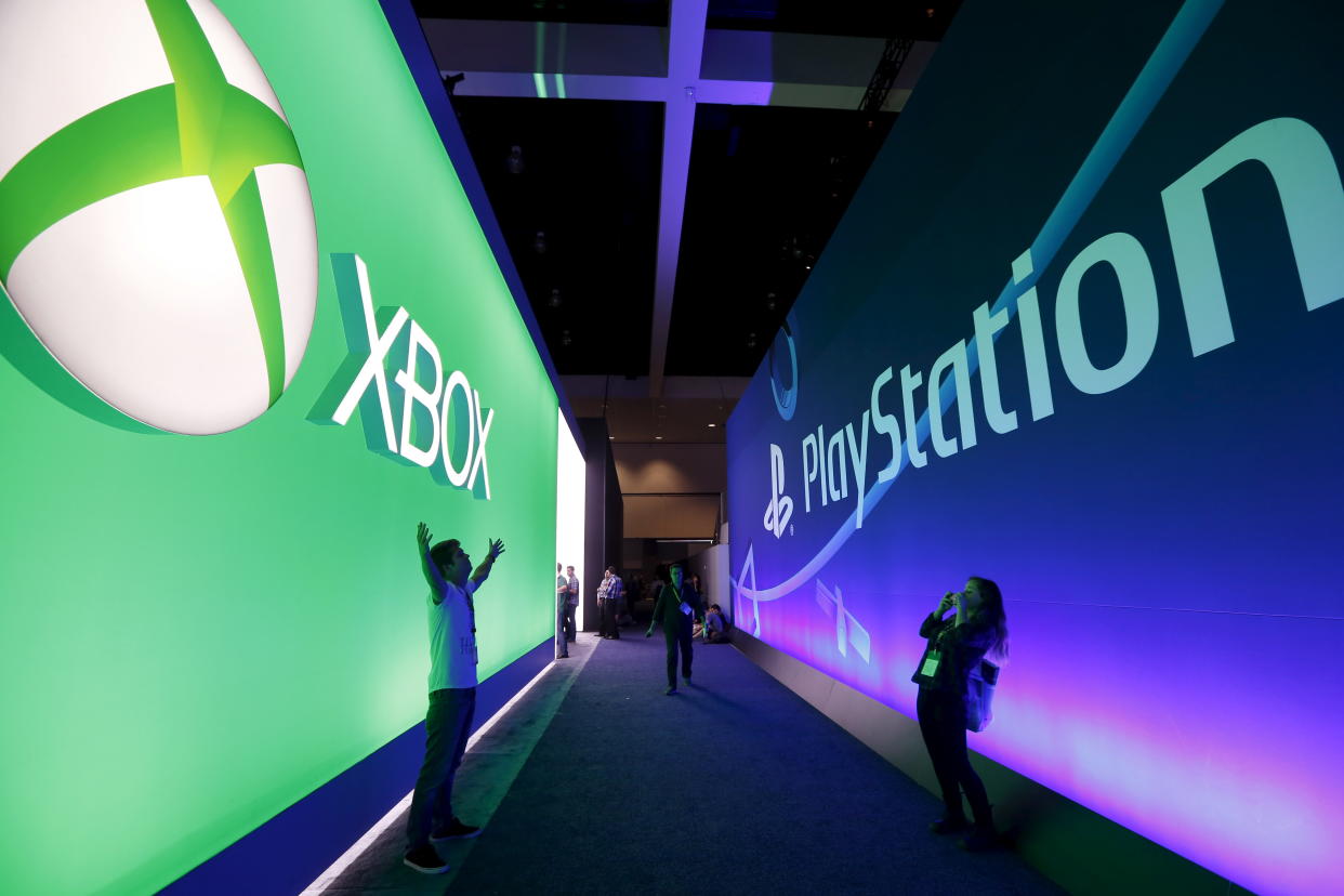 A man poses for a photo in front of a Microsoft Xbox sign opposite a Sony PlayStation sign at the Electronic Entertainment Expo, or E3, in Los Angeles, California, United States, June 16, 2015. REUTERS/Lucy Nicholson 