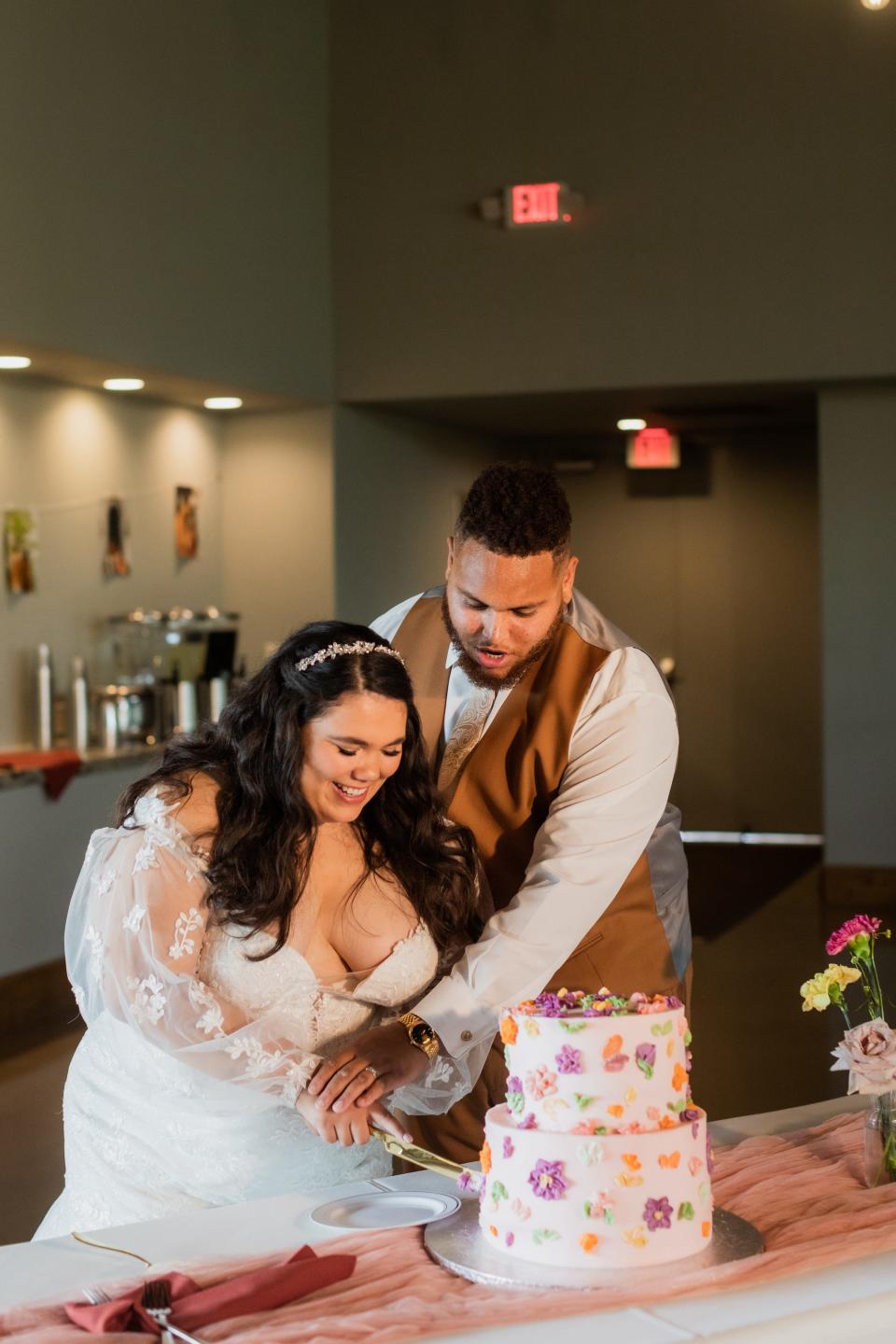 A bride and groom cut their wedding cake, which is covered in flowers.