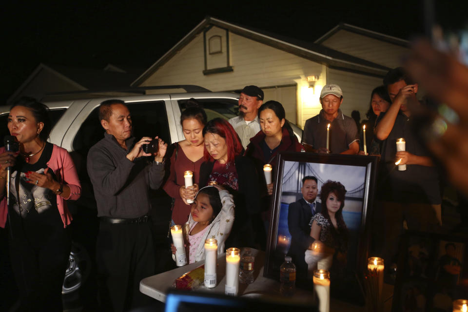 In this photo taken Monday, Nov. 18, 2019, the wife and young daughter of shooting victim Kou Xiong stand among the crowd during the candle light vigil in his honor outside their home in Fresno, Calif. A close-knit Hmong community was in shock after gunmen burst into a California backyard gathering and shot 10 men, killing four. "We are right now just trying to figure out what to do, what are the next steps. How do we heal, how do we know what's going on," said Bobby Bliatout, a community leader. (Larry Valenzuela/The Fresno Bee via AP)