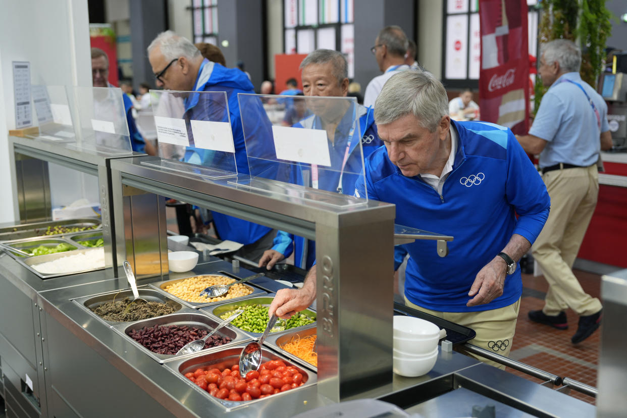 CORRECTION / German International Olympic Committee (IOC) President Thomas Bach tries food from a salad bar while touring at the Olympic Village, in Saint-Denis near Paris on July 22, 2024, ahead of the 2024 Paris 2024 Olympic Games (Photo by David Goldman / POOL / AFP) / 