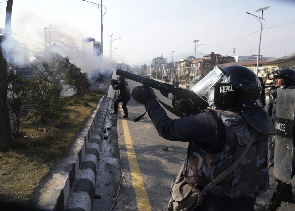 A Nepalese policeman fires tear gas as protesters opposing a proposed U.S. half billion dollars grant for Nepal clash with them as the parliament debates the contentious aid in Kathmandu, Nepal, Sunday, Feb. 20, 2022. Opposition to the grant comes mainly from two Communist parties that are part of the coalition government who claim the conditions in the grant agreement will prevail over Nepal's laws and threaten the country's sovereignty. (AP Photo/Niranjan Shreshta)