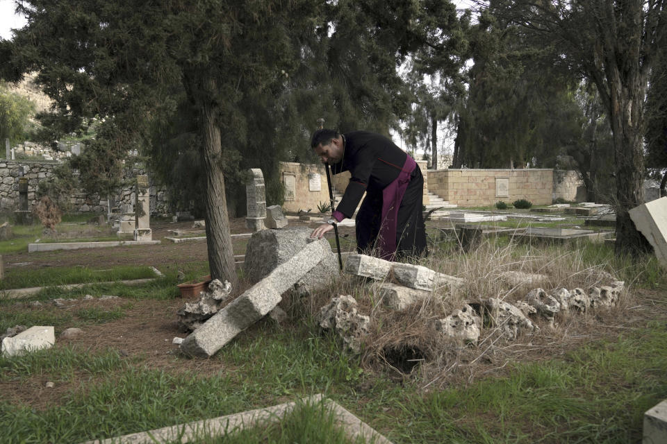 Hosam Naoum, a Palestinian Anglican bishop, touches a damaged grave where vandals desecrated more than 30 graves at a historic Protestant Cemetery on Jerusalem's Mount Zion in Jerusalem, Wednesday, Jan. 4, 2023. Israel's foreign ministry called the attack an "immoral act" and "an affront to religion." Police officers were sent to investigate the profanation. (AP Photo/ Mahmoud Illean)