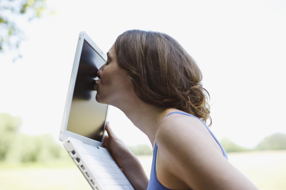 A woman kissing a laptop while holding it up.