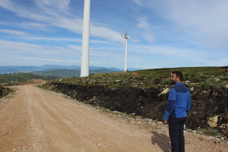 The author stood on a road next to a bank of excavated peat and two wind turbines.