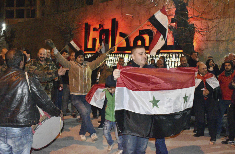In this photo released by the Syrian official news agency SANA, Syrians celebrate as they hold their national flags in Aleppo province, Syria, Monday, Feb. 17, 2020. On Monday Syria's military announced its troops have regained control of territories in northwestern Syria "in record time," vowing to continue to chase armed groups "wherever they are." (SANA via AP)
