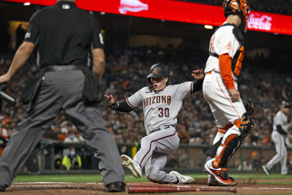 Arizona Diamondbacks' Jake McCarthy (30) slides home safely on Josh Rojas's sacrifice fly to left field as San Francisco Giants catcher Buster Posey (28) waits for the relay. during the third inning of a baseball game, Tuesday, Sept. 28, 2021, in San Francisco. Umpire is Scott Barry. (AP Photo/D. Ross Cameron)