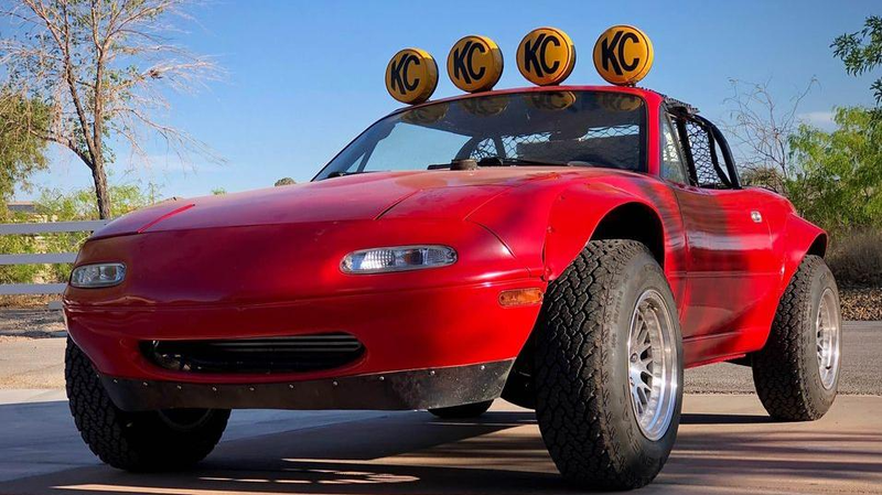 Mazda Miata lifted for off-road use. Yellow rally lights adorn the roof. 