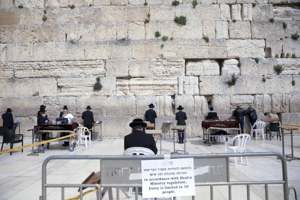 FILE - In this March 15, 2020, file photo Ultra Orthodox Jews practicing social distancing pray at the Western Wall in Jerusalem. The coronavirus pandemic has much of the world contemplating an existential question amid a growing number of stay-at-home orders, with only "essential" service providers allowed to go to their jobs. As U.S. states enact sweeping stay-at-home orders, there is lots of agreement on what's essential, but some have their own notions. A few are eyebrow raisers. Among them are guns, golf and cannabis. Most lists, being compiled by governors and others, capture the basics of what's essential. (AP Photo/Mahmoud Illean, File)