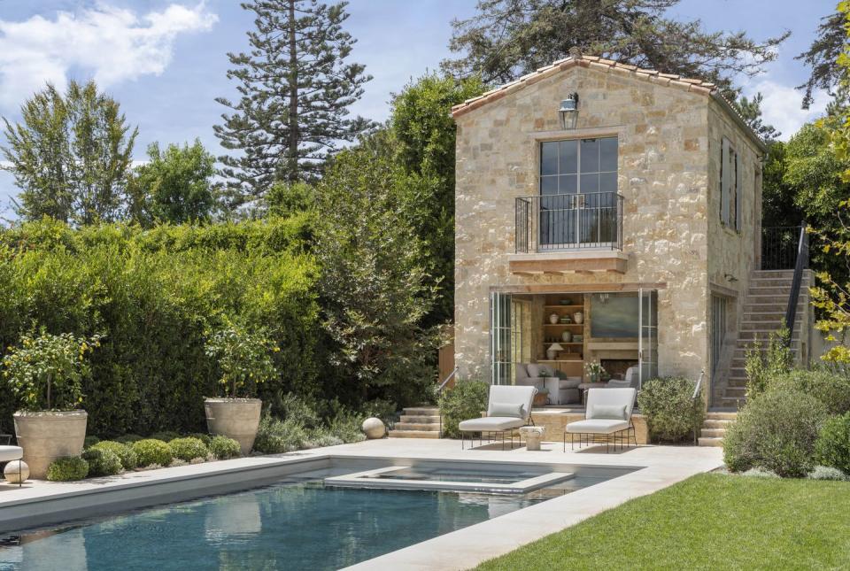 a stone pool house that is two stories and a rectangle pool in california