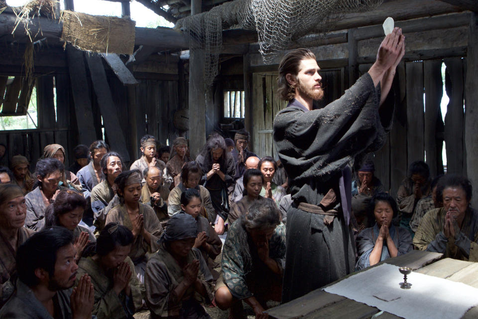 Andrew Garfield holds up communion bread while others pray