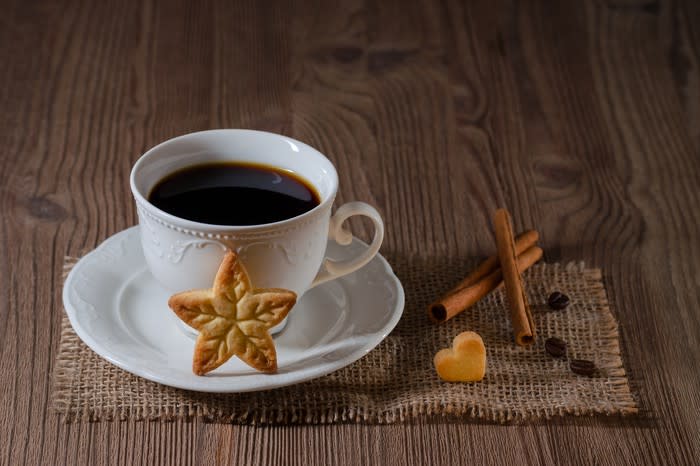 Filled coffee cup on a placemat with a star cookie in front and a heart cookie at the side.