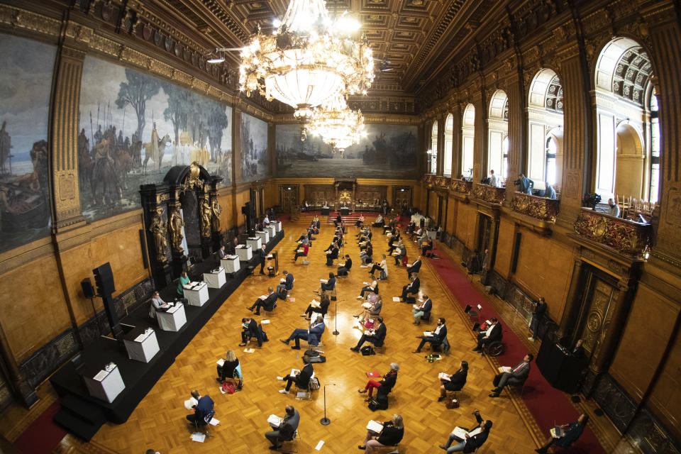 Peter Tschentscher, behind the speaker's desk, first Mayor of Hamburg, speaks at a government declaration on the topic "Current Coronalage - First Steps into a Normal Life" at a meeting of the Hamburg Parliament in the city hall in Hamburg, Germany, Wednesday, April 22, 2020. To avoid contagion among the members of parliament, the citizens' meeting will take place in the Great Festival Hall of the City Hall, spectators are not allowed. (Christian Charisius/dpa via AP)