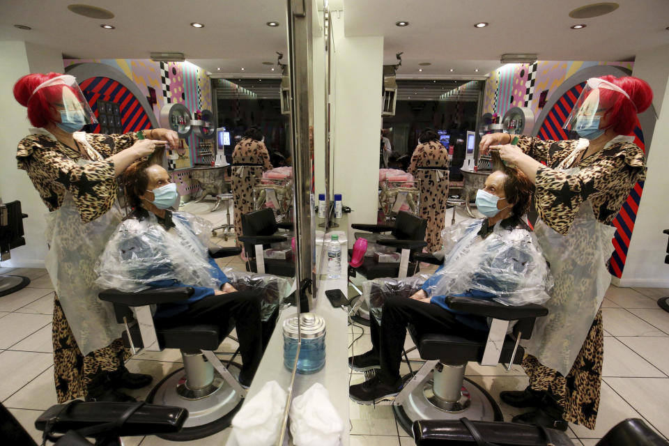 CORRECTS STYLIST'S NAME - Carole Rickaby cuts the hair of customer Sandra Jacobs at Tusk Hair in Camden, London, after opening at midnight to the first post-lockdown customer as restrictions are eased across England early Saturday, July 4, 2020. The easing of restrictions, which were imposed on March 23, allows businesses including pubs, restaurants and hair salons, to reopen to members of the public with measures in place to prevent the spread of the coronavirus. (Jonathan Brady/PA via AP)