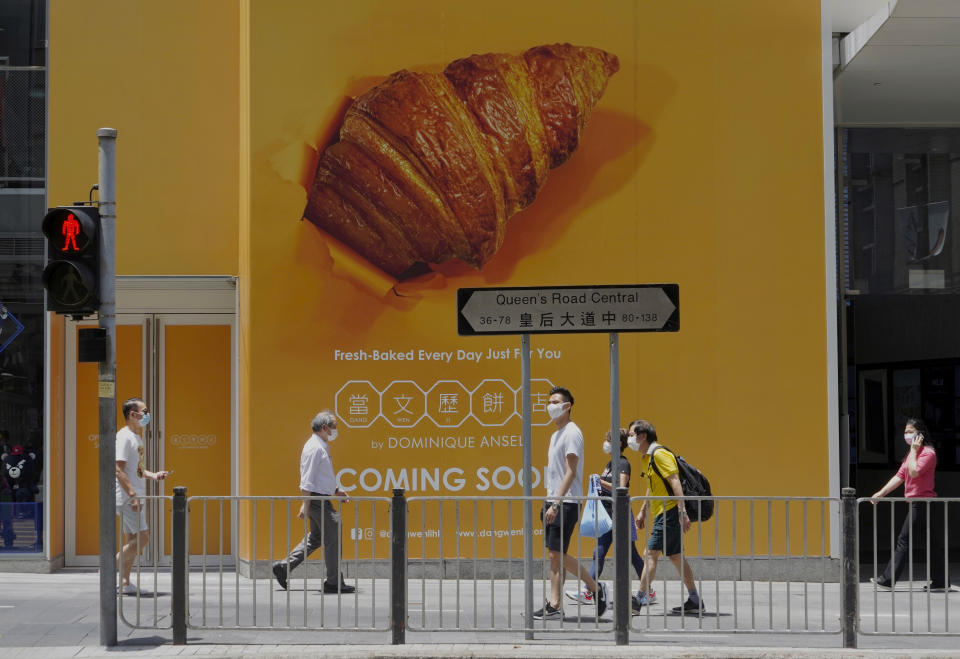 People wearing face masks to prevent the spread of the coronavirus walk past an advertising poster in Hong Kong, Wednesday, May 5, 2021. (AP Photo/Vincent Yu)