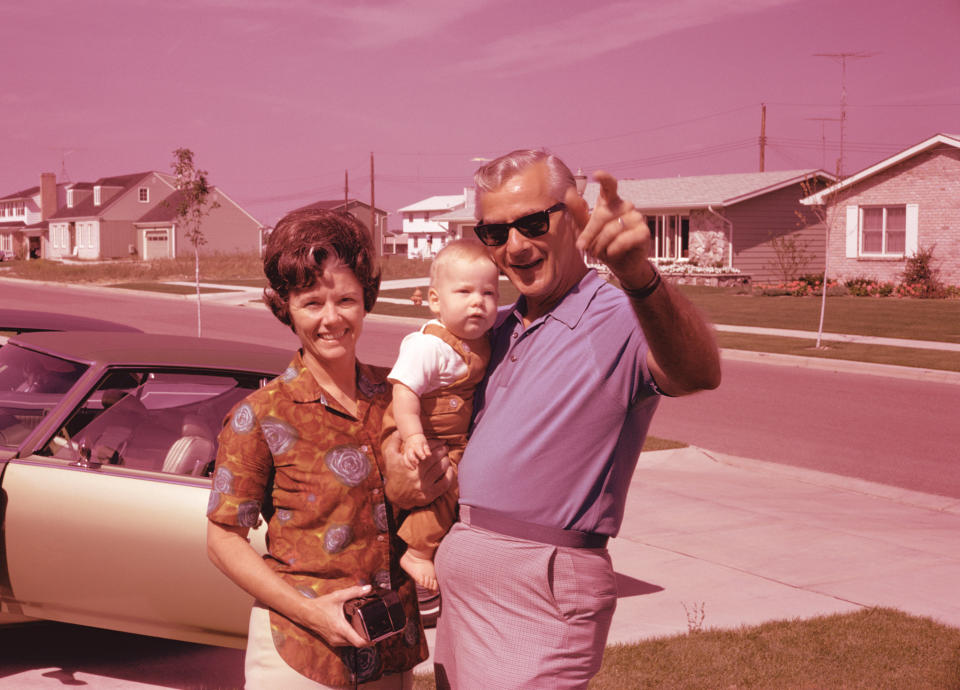 A family standing in a suburban neighborhood, with a man holding a baby and pointing, and a woman holding an item. Retro style with a vintage car nearby