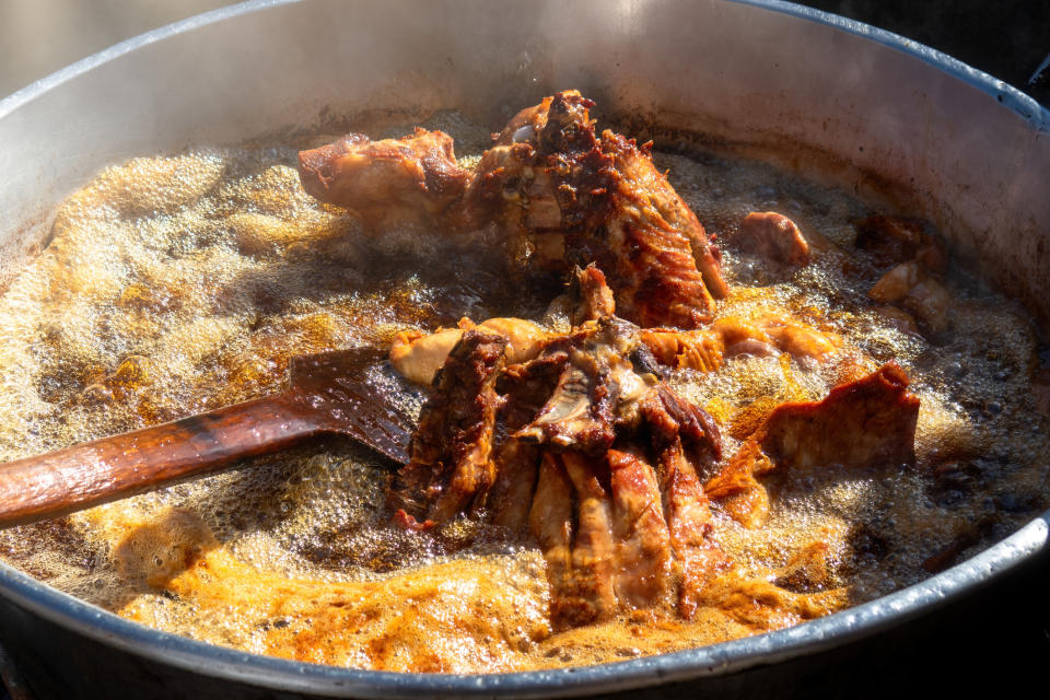 Large pot of frying chicken pieces with a wooden spatula