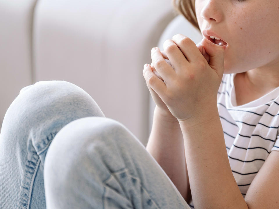 A girl sitting against a couch, coughing into her hands. She might have whooping cough. (Photo via Getty Images)